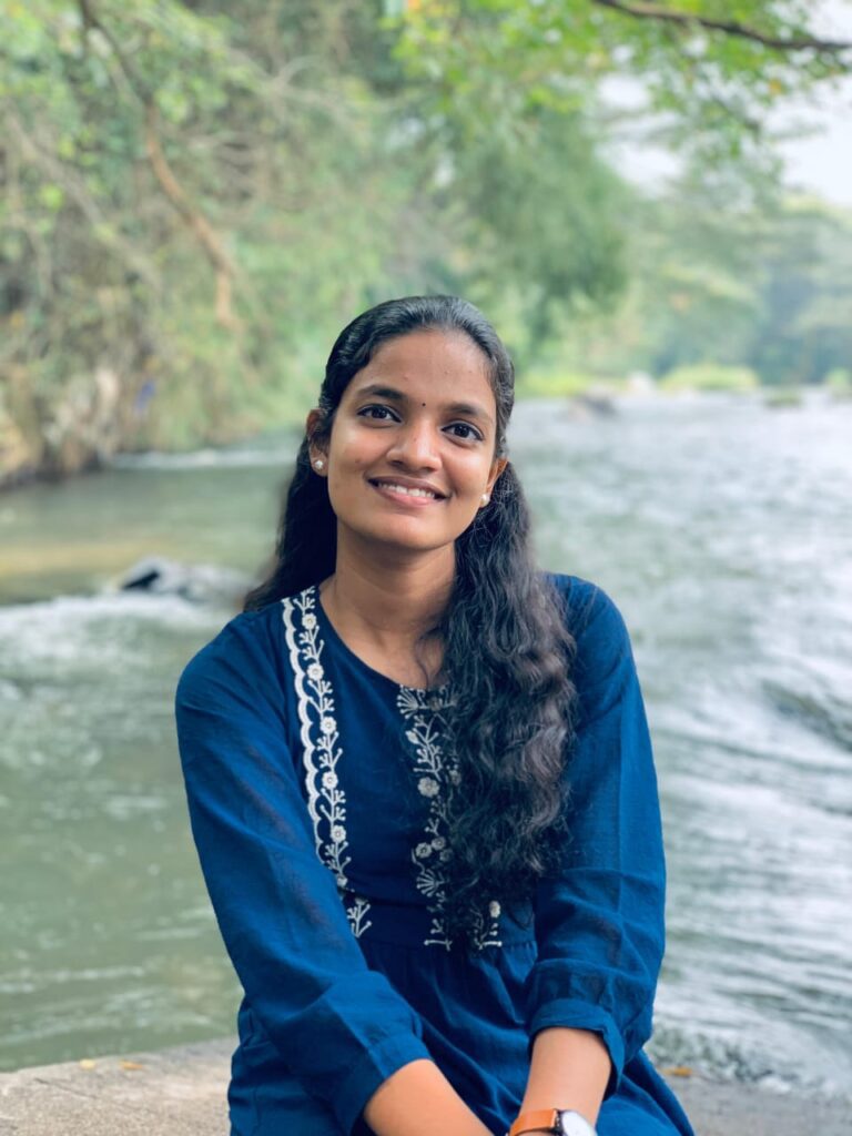 A young woman sits on a rock by a river, reflecting on her journey as a digital marketing freelancer in Kerala.