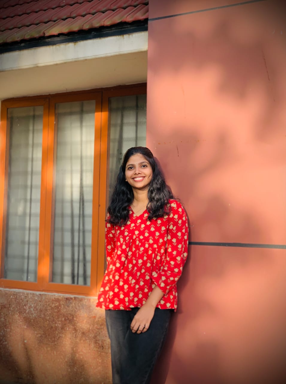 A woman in a red polka dot shirt stands confidently in front of a building, representing a digital marketing freelancer in Kerala.