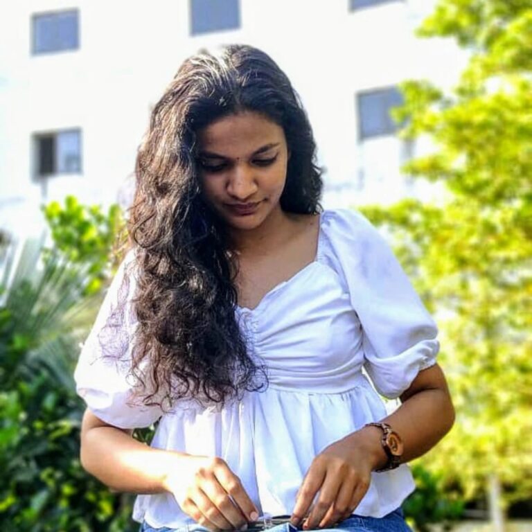 A woman in jeans and a white top checks her phone, representing the best digital marketing consultant in Kerala.