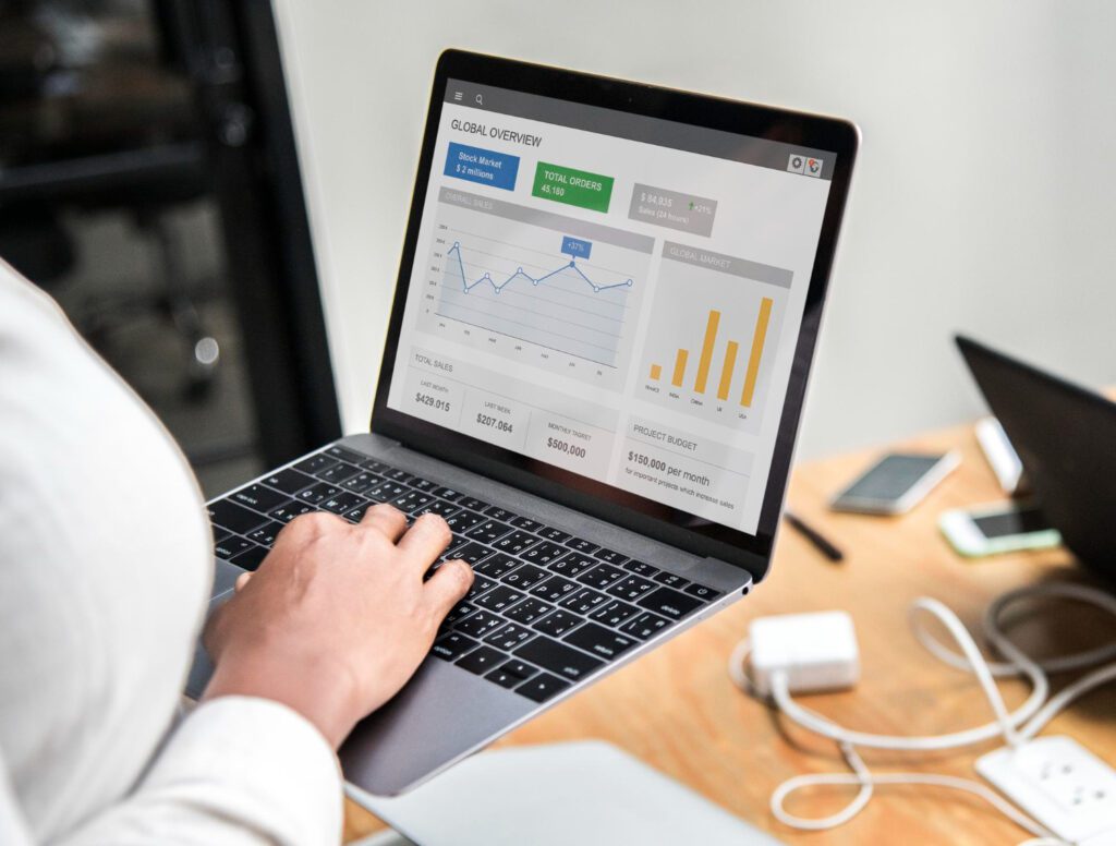 A person working on a laptop displaying analytics charts, sales reports, and marketing data dashboards in an office setting, representing a professional digital marketing expert in malappuram managing business growth and online performance.